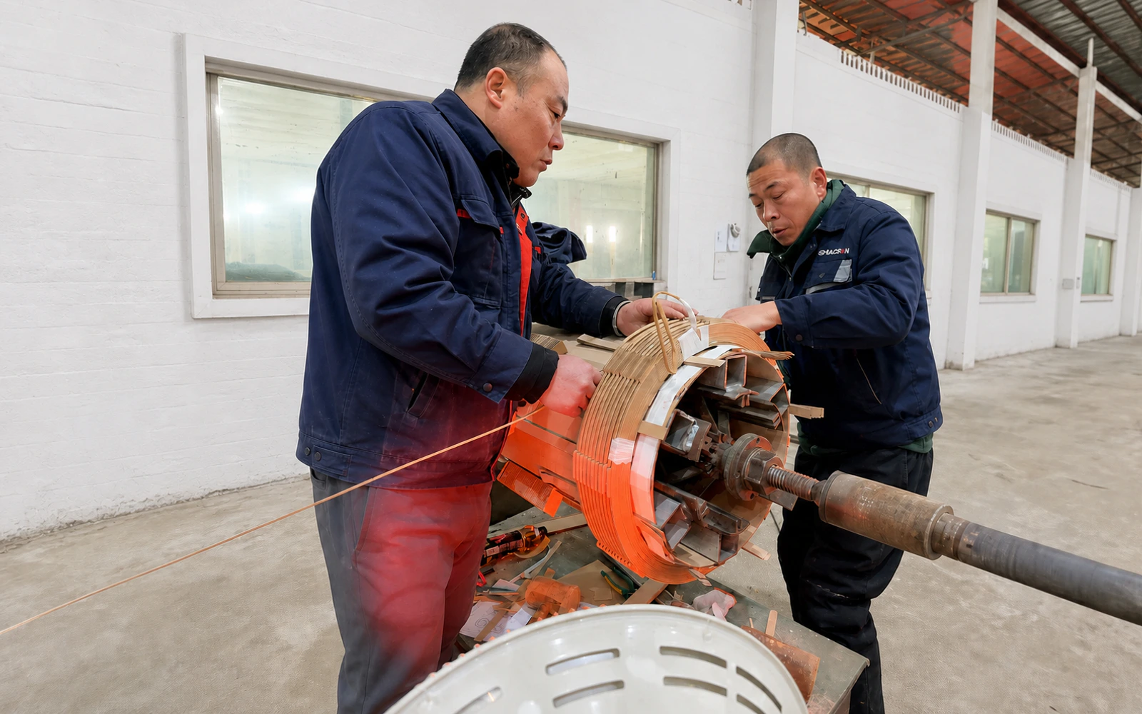 Operator performing transformer coil winding against a white-painted workshop wall